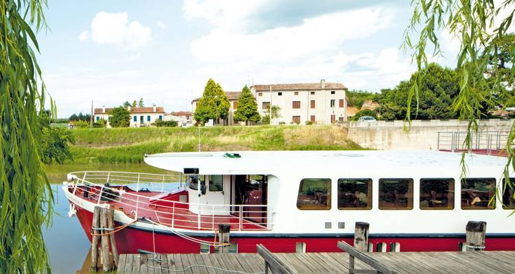Barco rojo y blanco atracado en un río tranquilo con vegetación.