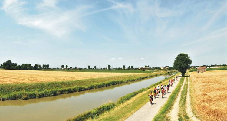 Ciclistas pedaleando junto a un canal tranquilo.