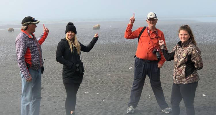 Quatre personnes pointant vers des ours sur une plage brumeuse.