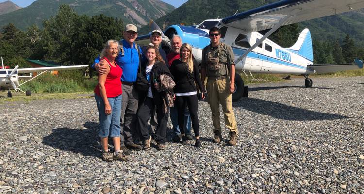 Groupe de touristes posant devant un petit avion sur un terrain rocheux.