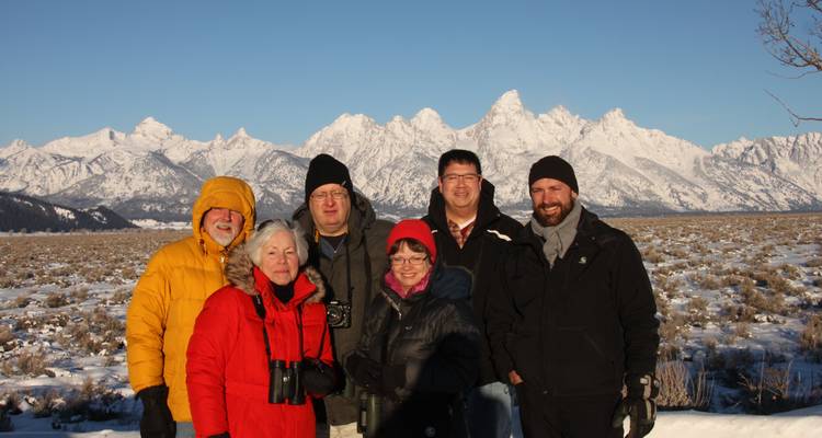 Petit groupe de touristes pose avec des jumelles devant les Tetons enneigés sous un ciel dégagé.