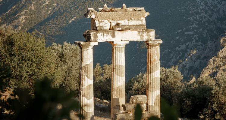 El Tholos de Delfos bañado en la cálida luz del atardecer contra las escarpadas laderas montañosas.