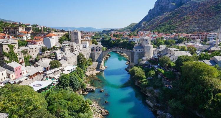 Vista panorámica del histórico puente de piedra Stari Most de Mostar arqueándose sobre el río Neretva de color esmeralda flanqueado por edificios medievales.