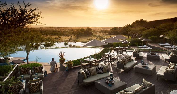 Outdoor lounge area overlooking a vast savannah landscape at sunset.