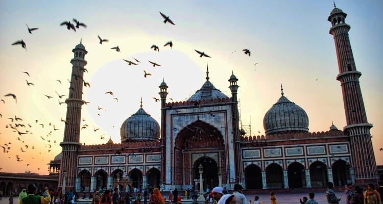 Zwermen duiven cirkelen boven Delhis Jama Masjid terwijl de ondergaande zon de koepels en minaretten tegen het licht uitlicht.