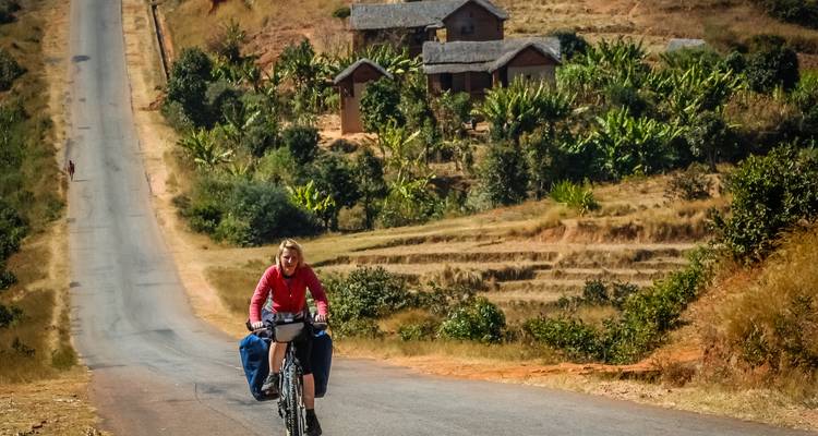 Persona andando en bicicleta por una carretera rural pintoresca con cabañas al fondo.