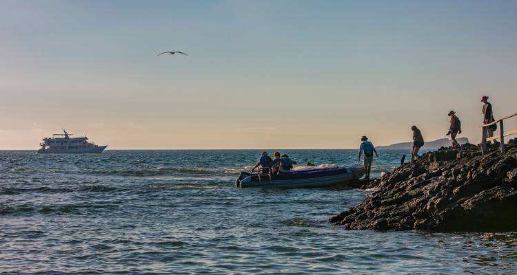 Des gens débarquant d'un petit bateau sur un rivage rocheux.