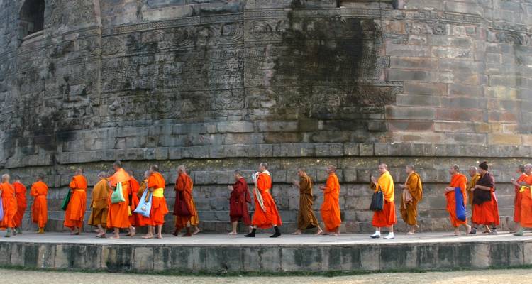 Mönche in orangefarbenen Roben, die in einer Reihe um eine Stupa gehen.