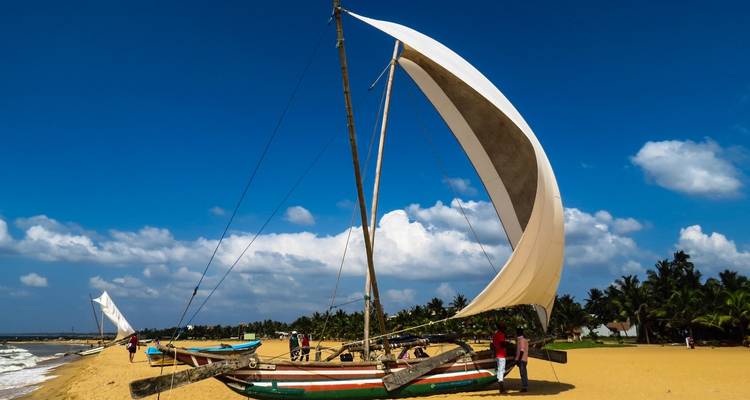 Bateau de pêche traditionnel avec une grande voile sur une plage ensoleillée.