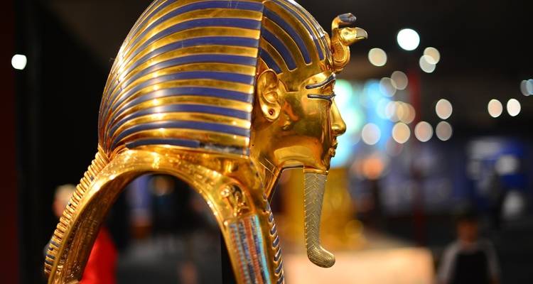 Una máscara dorada de faraón con grabados intrincados y colores exhibida en un museo.