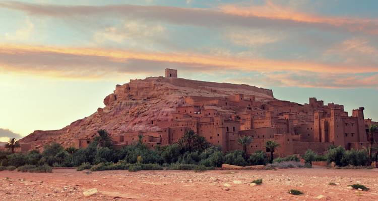 Ait Benhaddou, a historic fortified village with clay buildings set against a vibrant sunset sky.