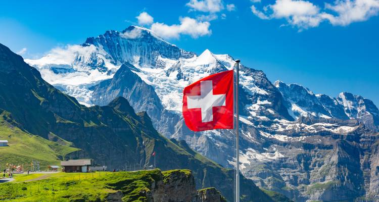 Drapeau suisse flottant au sommet d'une crête herbeuse contre des pics enneigés spectaculaires dans les Alpes bernoises.