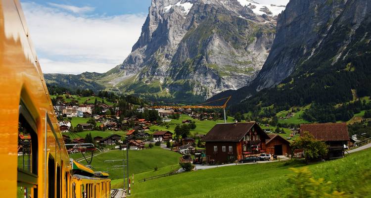Train de montagne jaune serpentant à travers de verts pâturages vers les Alpes dentelées près de Grindelwald.
