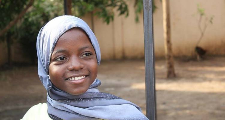 A portrait of a smiling girl wearing a headscarf.