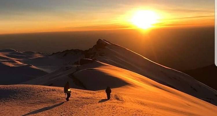 Coucher de soleil sur une montagne enneigée avec des personnes qui marchent.