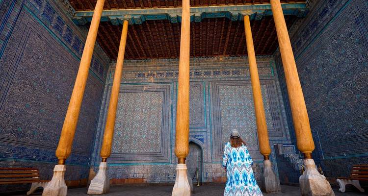 Murs aux motifs complexes avec de hauts piliers en bois, une personne contemplant la décoration.