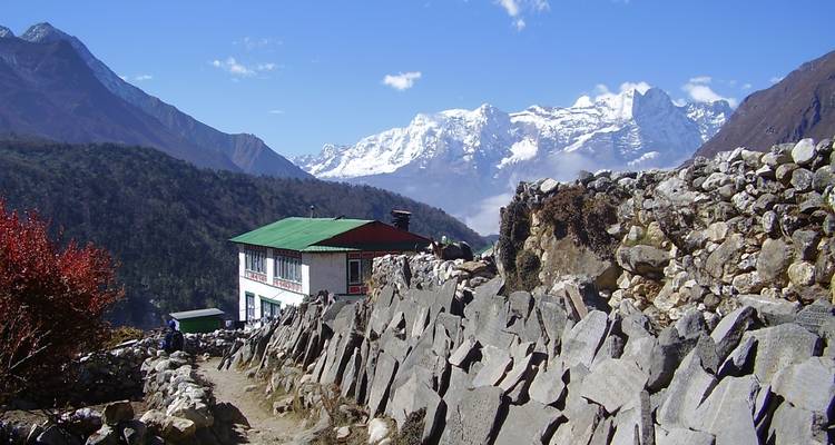 Maison traditionnelle entourée de murs de pierre et de montagnes enneigées.