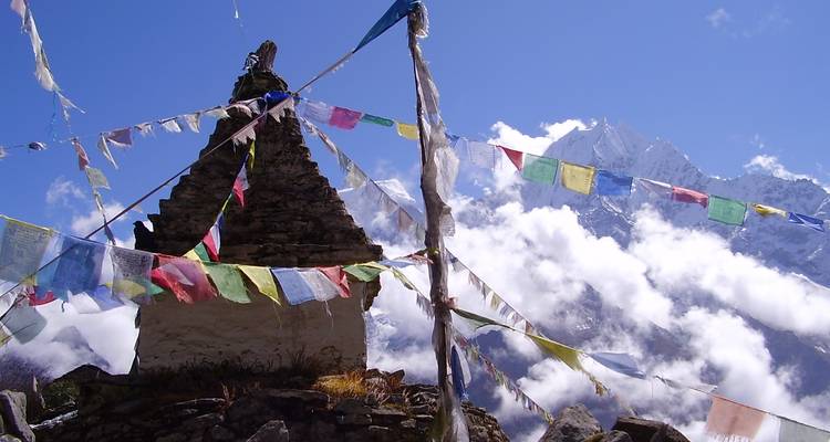 Drapeaux de prière colorés devant des montagnes partiellement obscurcies par les nuages.