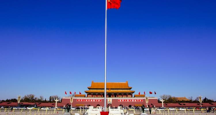 Plaza de Tiananmén con un imponente asta de bandera roja y la Puerta de la Paz Celestial bajo un cielo despejado.