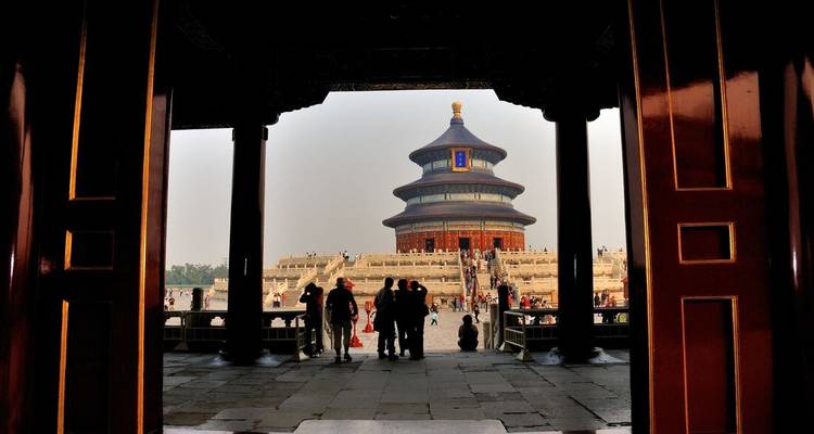Templo del Cielo enmarcado por puertas de madera con visitantes en la amplia plataforma de piedra.