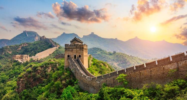 Torre de la Gran Muralla bañada en la luz dorada del amanecer con exuberantes crestas verdes extendiéndose hacia la distancia.