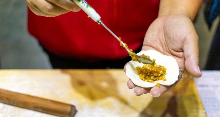 Primer plano de manos rellenando una masa de dumpling con mezcla salada.