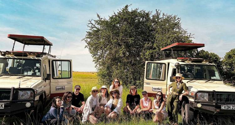 Groupe de personnes avec des véhicules de safari dans un environnement de prairie.