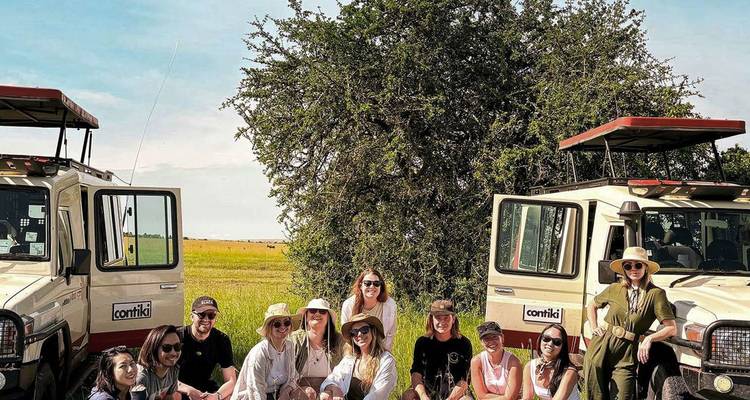 Un grupo de turistas se arrodilla entre dos vehículos de safari en una llanura abierta de Kenia listos para la aventura de vida silvestre.