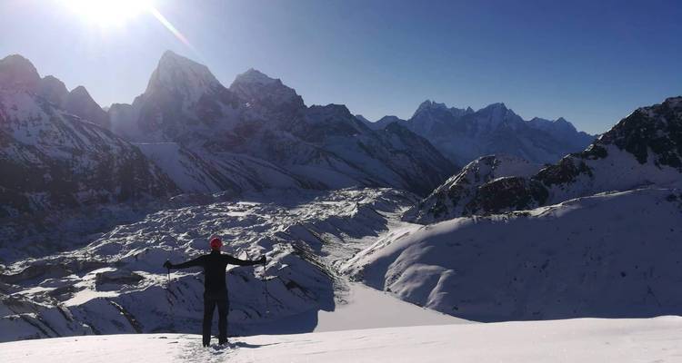 Personne les bras étendus contemplant un paysage montagneux enneigé.
