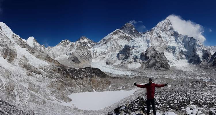Personne avec les bras étendus devant une chaîne de montagnes enneigées.