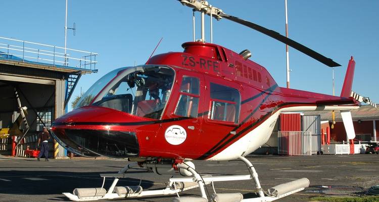 Hélicoptère rouge garé au sol avec un hangar en arrière-plan.