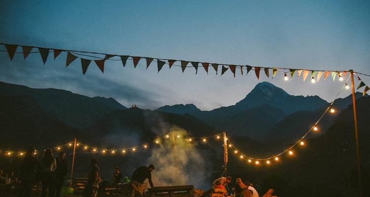 Rassemblement en plein air avec montagnes et guirlandes lumineuses en arrière-plan.