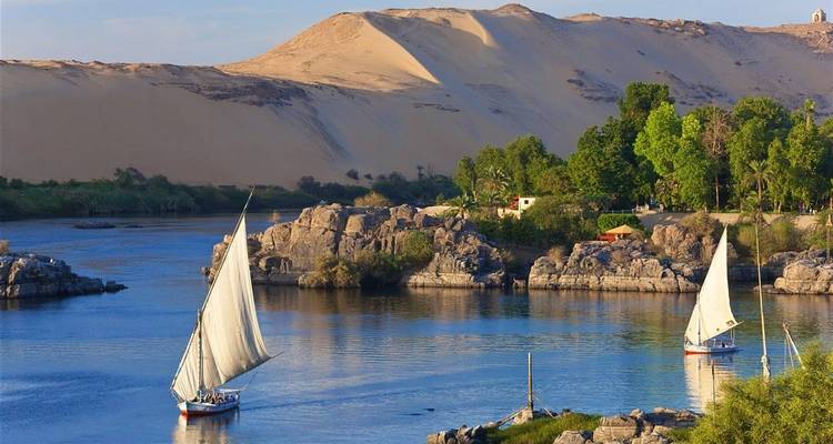 Sailboats on a river with a sandy hill in the background.
