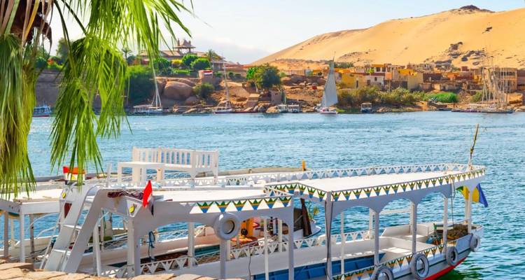 Traditional boats on a river with a desert and village in the background.