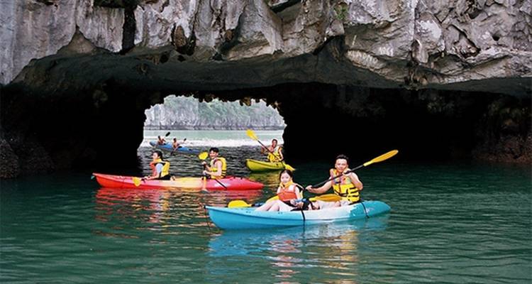 Group of kayakers paddling under a cave in a picturesque setting.