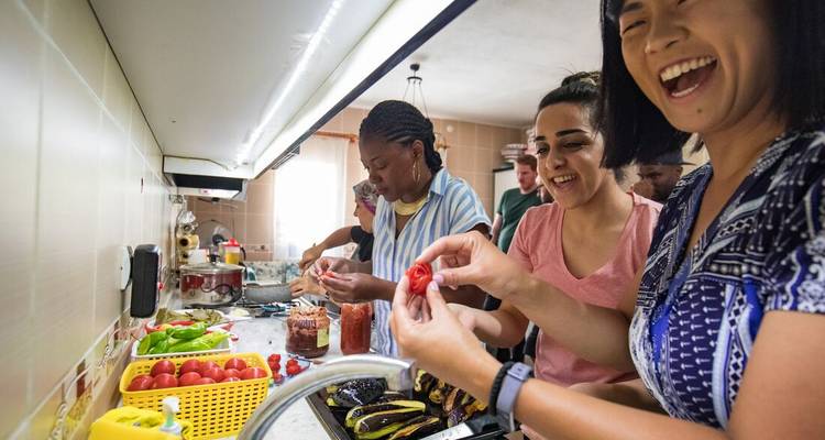 Viajeros sonrientes preparan comida juntos en una cocina hogareña durante una clase de cocina.