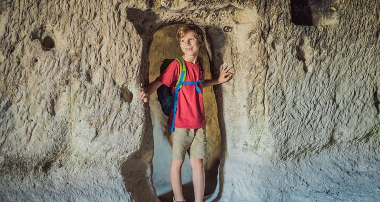 Un niño con mochila explora una entrada estrecha tallada en roca blanda de cueva.