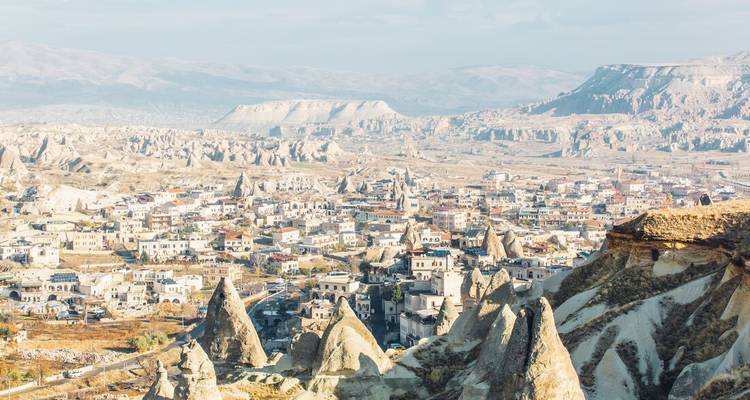 Vista aérea amplia de las agujas del pueblo de Capadocia y las chimeneas de hadas extendiéndose a través de un valle iluminado por el sol.