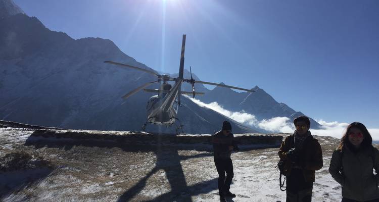 Helicopter on a snowy landing pad with people around and distant mountains.