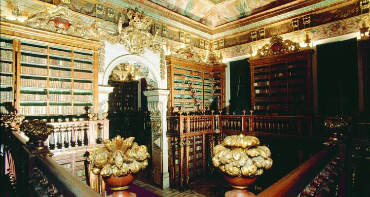 Lujoso salón de biblioteca barroca with estanterías de madera ornamentadas, detalles dorados y techo pintado en la Universidad de Coimbra.