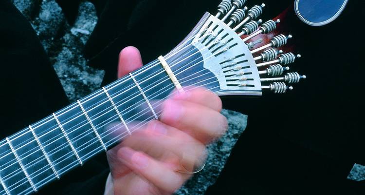 Primer plano de la mano de un músico tocando una guitarra portuguesa, mostrando las clavijas de afinación y las cuerdas en detalle.