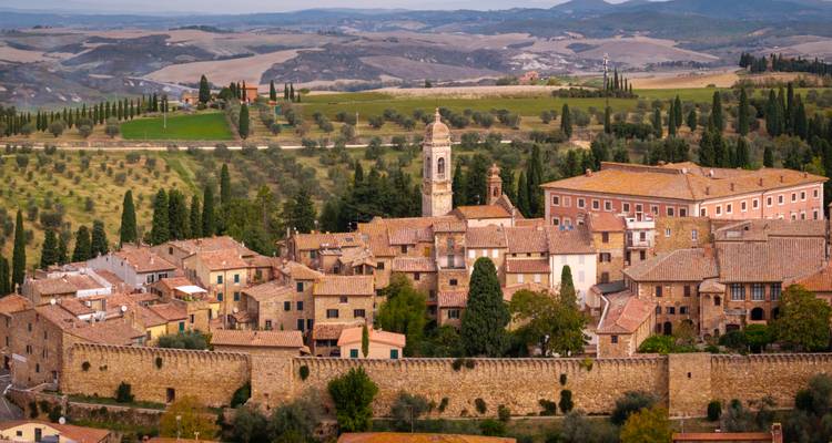 Ville toscane perchée sur une colline, entourée de cyprès et de la campagne vallonnée de la Val d'Orcia.