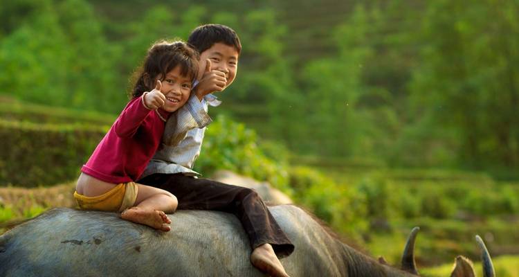 Deux enfants souriants qui font un signe de pouce en l'air assis sur un animal.