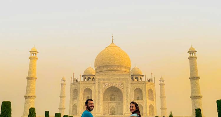Deux personnes souriant devant le Taj Mahal au coucher du soleil
