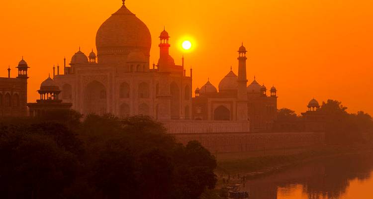 Schattenriss des Taj Mahal und der umgebenden Minarette mit einem leuchtend orangefarbenen Sonnenaufgang, der dramatisches Licht wirft.