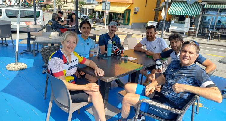 Fietsgroep ontspant zich in een openluchtcafé, lachend rond een beschaduwde tafel.