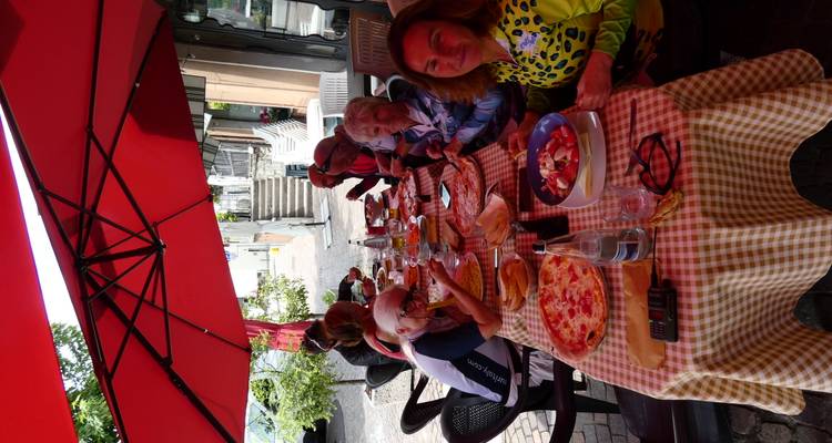 Groep diners geniet van pizza en salade onder felrode terrasoverkappingen.