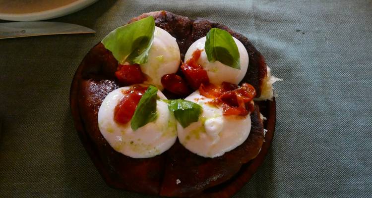 Gourmetbordje burrata afgetopt met vers basilicum en tomaat op rustiek brood.