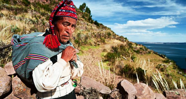 Persona indígena con vestimenta colorida en un paisaje montañoso.