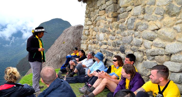 Grupo de excursionistas descansando junto a una estructura de piedra en una zona montañosa.